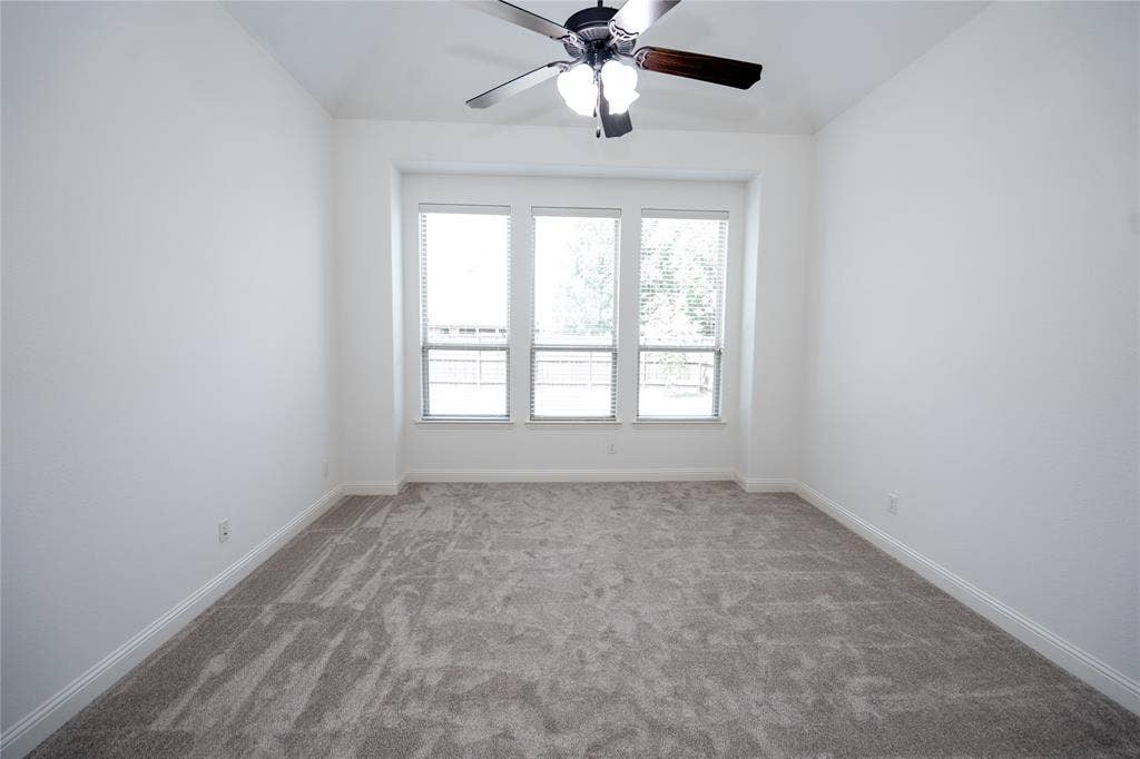 Recessed window bay, gray carpet, multiple windows with blinds, ceiling fan with light fixture, and white wall finishes