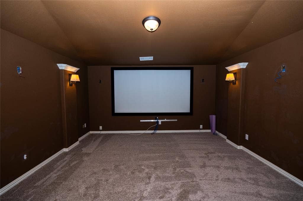 Dedicated media room featuring a large projection screen, built-in wall sconces, and recessed overhead lighting