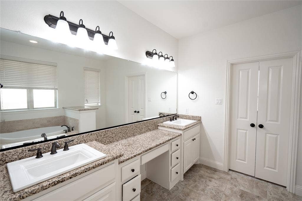 Dual vanity with granite countertops, integrated sinks, white cabinetry, and matte black hardware