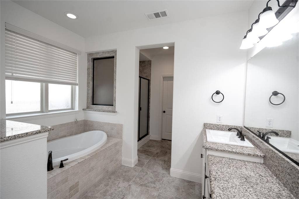 Bathroom featuring a built-in tub with tile surround, a dual vanity with granite countertops, and a walk-in shower with a glass enclosure