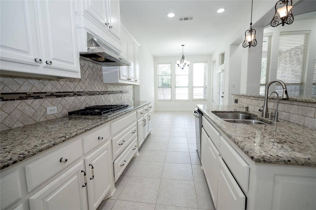 White cabinetry paired with granite countertops, a tiled backsplash, a stainless steel gas range with a coordinating hood, and a dual basin sink with a pull-down faucet