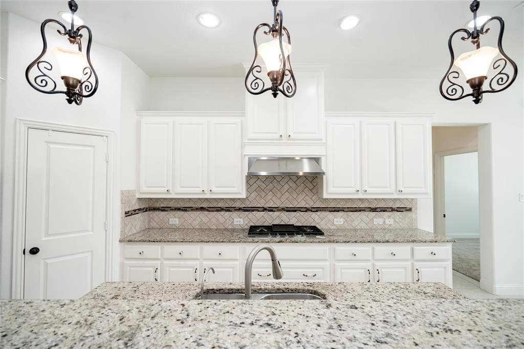 Kitchen featuring an island with a stainless steel sink and faucet, white cabinetry, granite countertops, and a herringbone tile backsplash