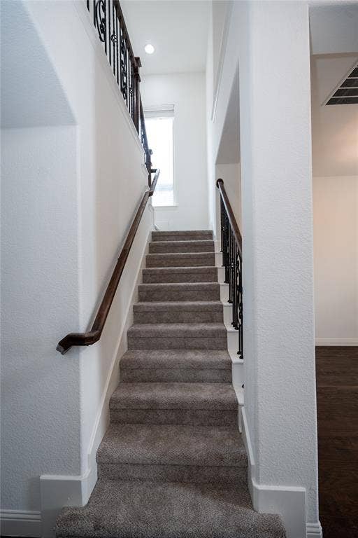Carpeted staircase featuring wrought iron balusters and a dark wood handrail