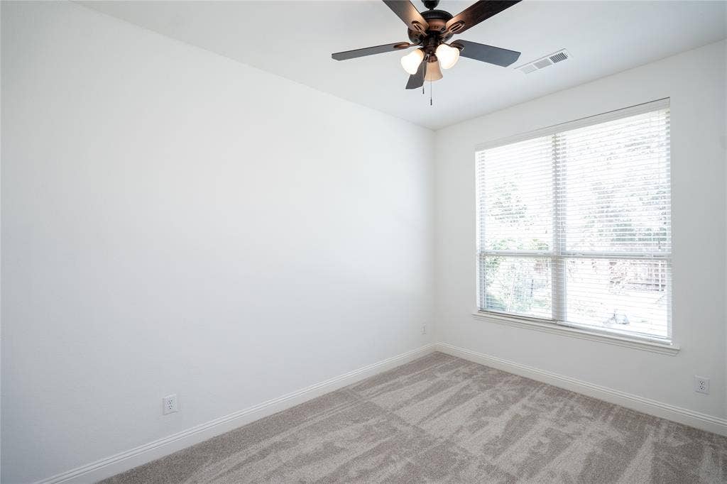 Spacious room with plush carpeting, a large window, a ceiling fan with integrated lighting, and crisp white walls