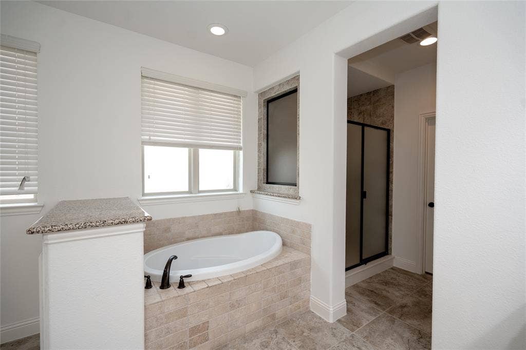 Recessed bathtub with tile surround, dual windows, granite-finish ledges, and a separate shower enclosure with frosted glass