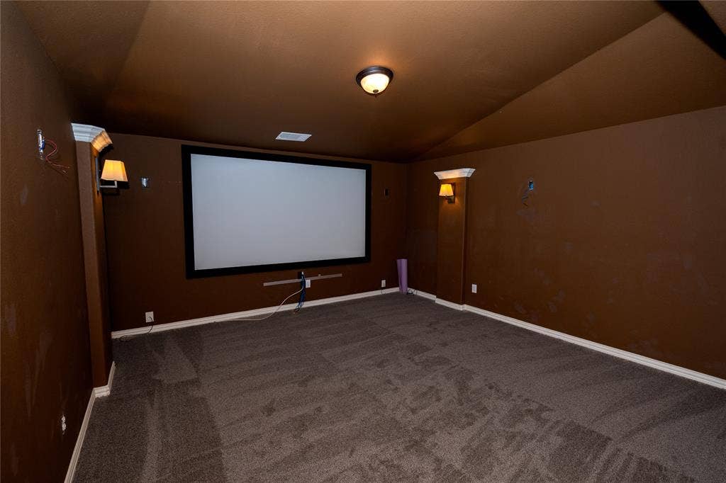 Dedicated media room featuring a large projector screen, wall sconces, and recessed overhead lighting