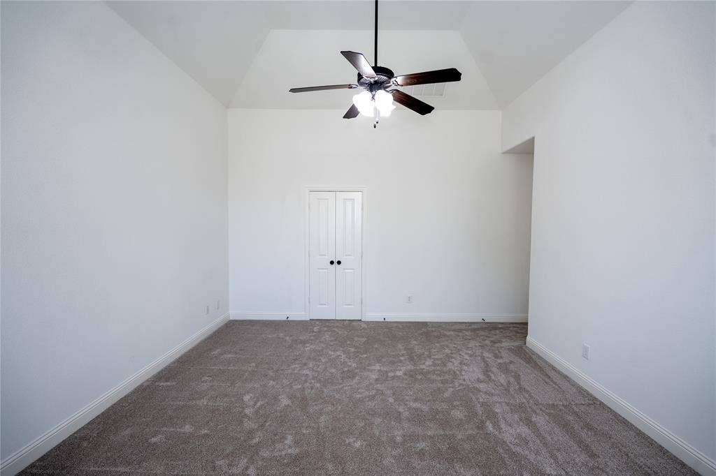 Vaulted ceiling featuring a ceiling fan, neutral carpeting, and white bi-fold doors