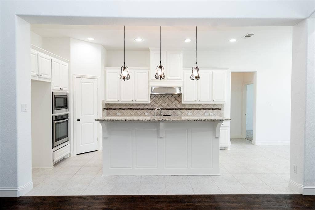 White cabinetry with stainless steel appliances, a kitchen island with pendant lighting, a tile backsplash, and light-toned tile flooring