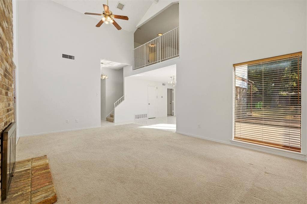 1512 Woodcreek Drive, Richardson, TX 75082 Vaulted ceiling with a ceiling fan, brick fireplace, carpeted flooring, and an upper-level balcony