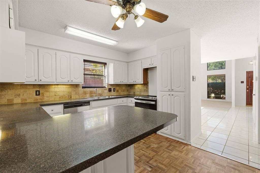 1512 Woodcreek Drive, Richardson, TX 75082 Kitchen with white cabinetry, dark countertops, tiled backsplash, and wood-finish flooring