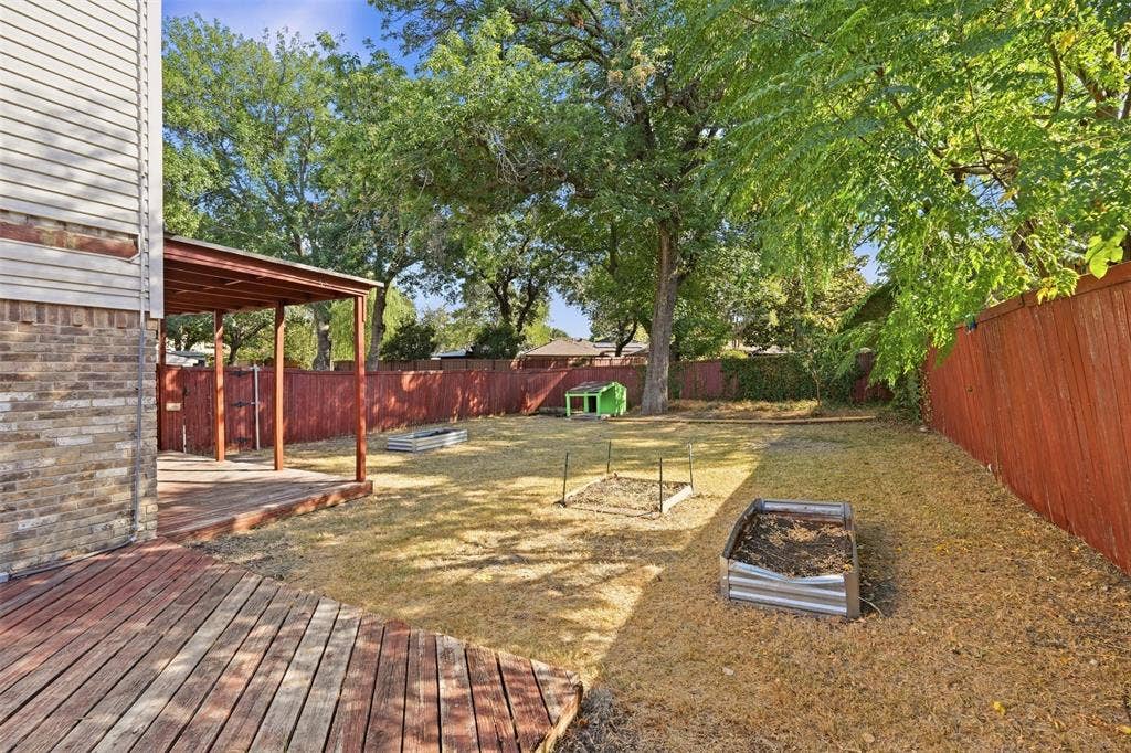 1512 Woodcreek Drive, Richardson, TX 75082 Expansive backyard featuring a covered patio, wood deck, privacy fence, and mature trees