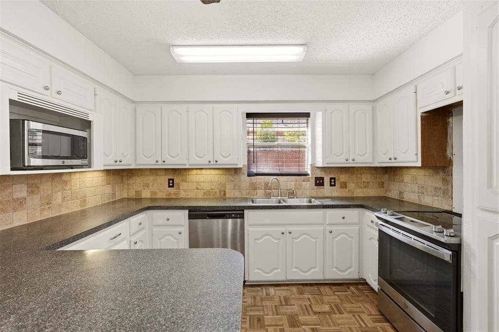 1512 Woodcreek Drive, Richardson, TX 75082 U-shaped kitchen featuring white cabinetry, stone-look countertops, stainless steel appliances, and a tiled backsplash