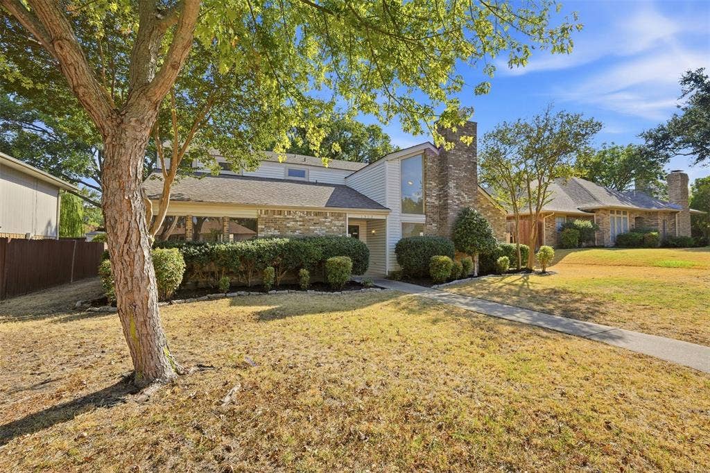 1512 Woodcreek Drive, Richardson, TX 75082 Front exterior featuring a brick and siding facade, prominent brick chimney, large window installation, and mature trees