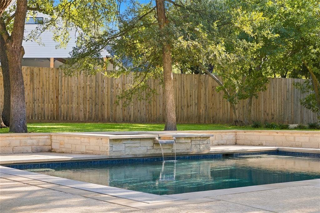 11408 Somerville Drive, Temple, TX 76502 Outdoor swimming pool with integrated spa and waterfall feature, surrounded by concrete decking and stone retaining walls