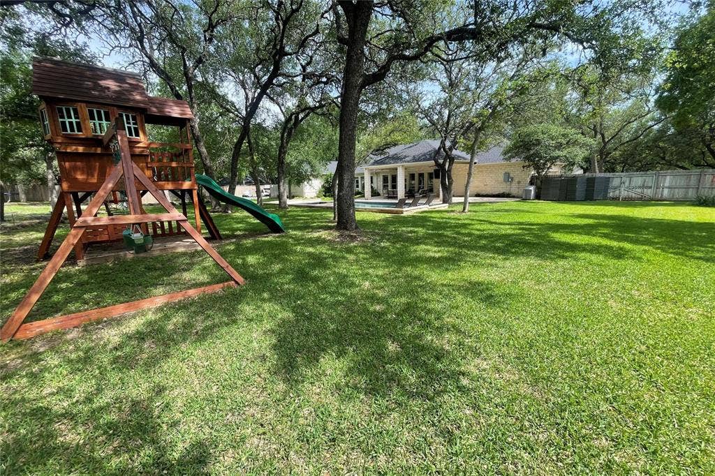 11408 Somerville Drive, Temple, TX 76502 Expansive backyard featuring a lush lawn, mature trees, and a wooden play structure with a slide