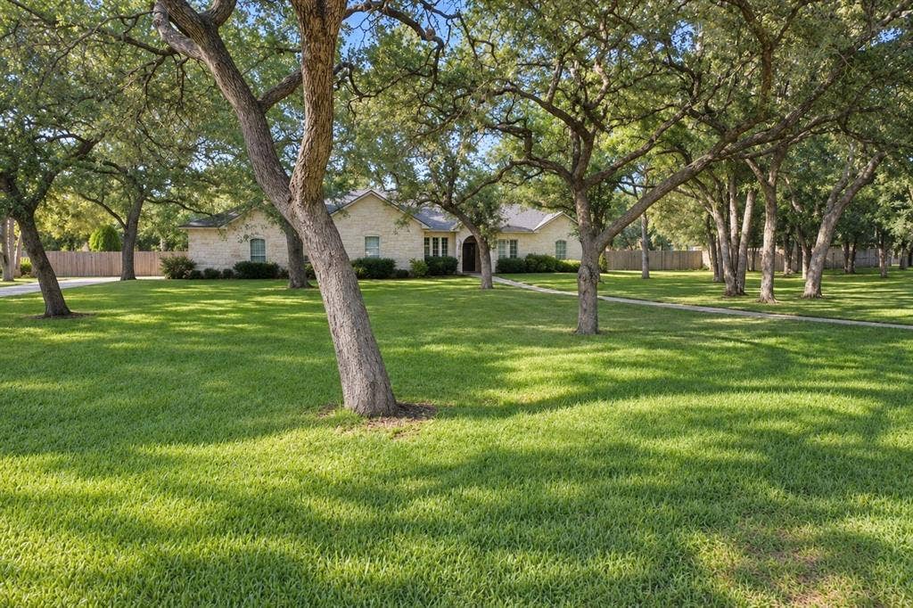11408 Somerville Drive, Temple, TX 76502 Expansive front lawn with mature trees, a stone exterior, and a paved walkway