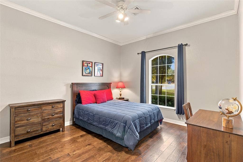 11408 Somerville Drive, Temple, TX 76502 Arch-top window with grid pattern, wood-finish flooring, ceiling fan with integrated lighting, crown molding, and a solid wood headboard