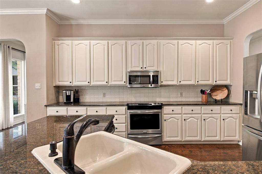 11408 Somerville Drive, Temple, TX 76502 White cabinetry with black hardware, stainless steel appliances, dark stone countertops, tile backsplash, and wood-finish flooring