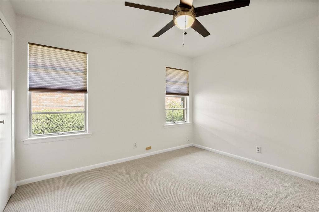 Neutral wall paint, textured carpet, two windows with blinds, ceiling fan with light fixture