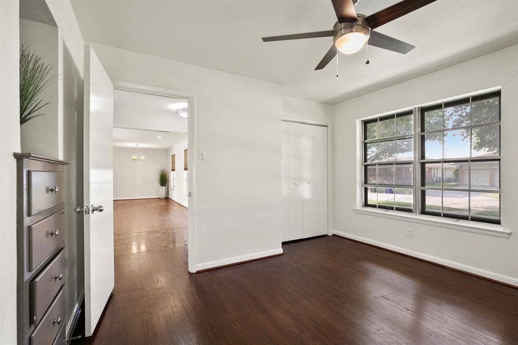 Hardwood flooring, crisp white walls, contemporary ceiling fan with integrated lighting, bi-fold closet doors, and large grid-pattern windows