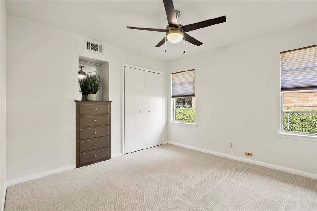 Plush carpet flooring, ceiling fan with integrated lighting, built-in dresser, bi-fold closet doors, and multiple windows with blinds