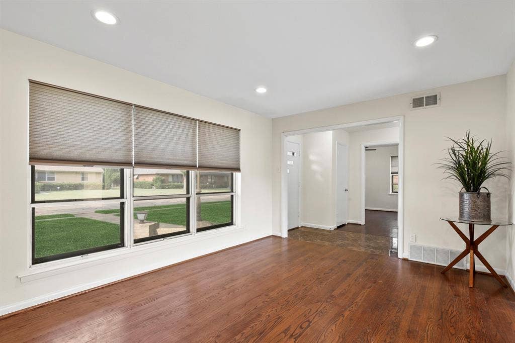 Rich wood-finish flooring, recessed ceiling lighting, bright window with blinds, and white interior walls