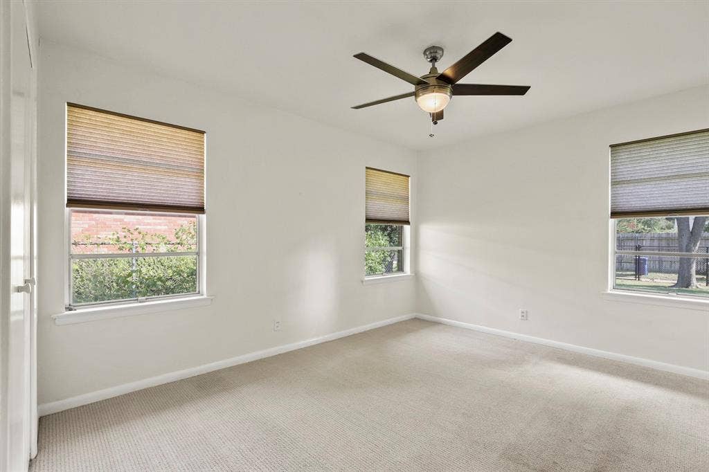 Neutral wall paint, three windows with cellular shades, ceiling fan with integrated lighting, and carpeted flooring