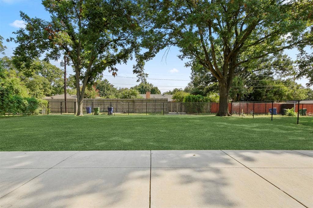 Expansive backyard featuring a manicured lawn, concrete patio, and mature trees