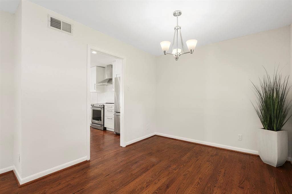 Hardwood flooring, contemporary chandelier, crisp white walls, and a recessed kitchen entry