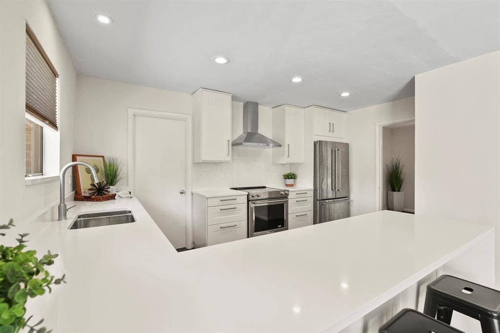 Kitchen featuring white cabinetry, stainless steel appliances, recessed lighting, and expansive countertops with an undermount sink