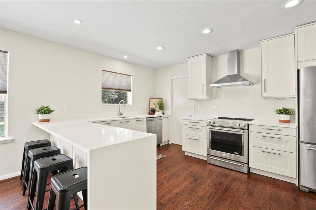 Kitchen featuring a breakfast bar with seating, white shaker-style cabinetry, stainless steel appliances, recessed lighting, and wood-finish flooring