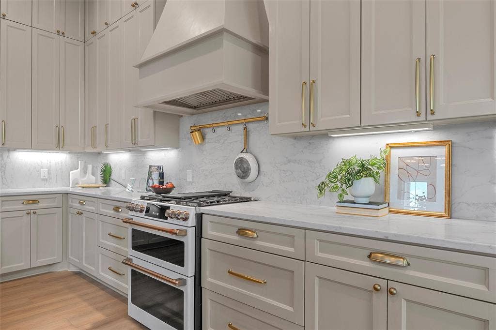 20 N Ritchie Road, Woodway, TX 76712 Light-toned cabinetry with gold-toned hardware, stone countertops, stone backsplash, under-cabinet lighting, and a double oven range with a coordinating vent hood