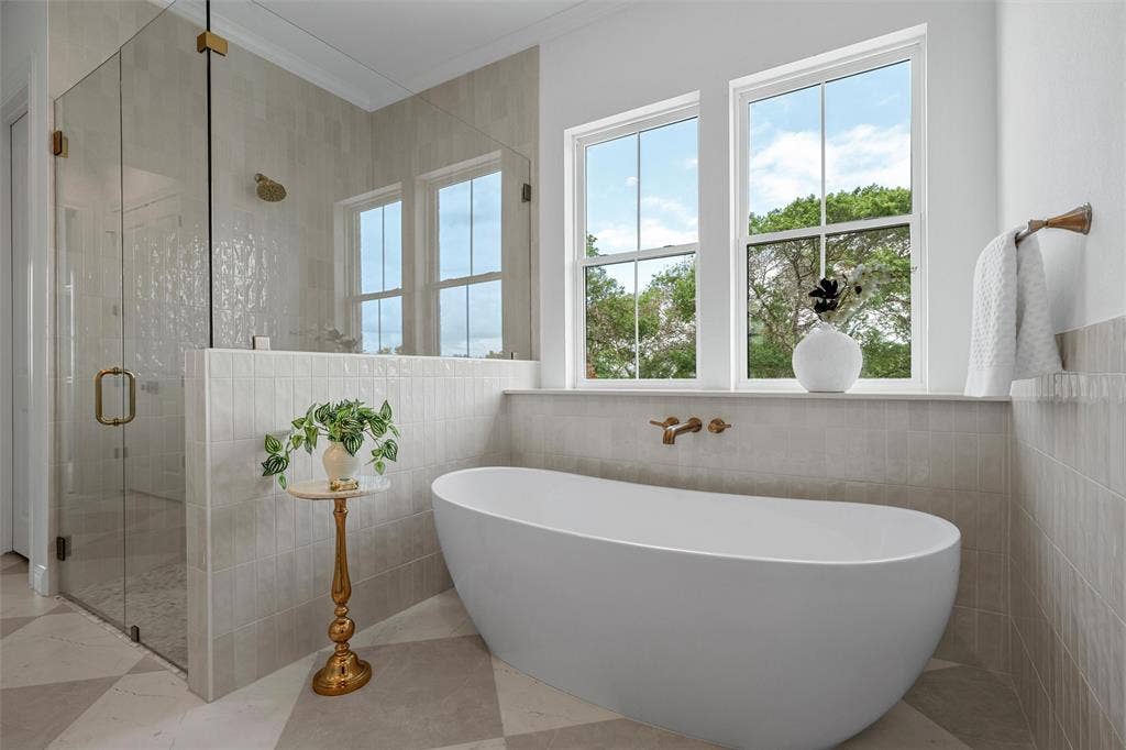 20 N Ritchie Road, Woodway, TX 76712 Freestanding soaking tub with wall-mounted fixtures, glass-enclosed shower with a rainfall showerhead, large double-hung windows, and checkerboard tile flooring