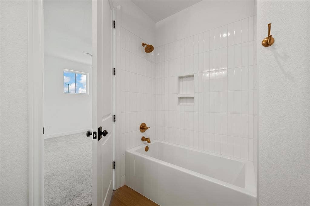 20 N Ritchie Road, Woodway, TX 76712 Bathtub with vertical white subway tile surround, recessed shelving, and brass fixtures