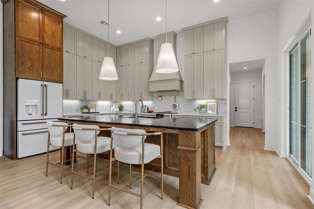 20 N Ritchie Road, Woodway, TX 76712 Kitchen featuring an expansive island with a dark countertop, light wood-finish flooring, two large pendant lights, and a full suite of white appliances