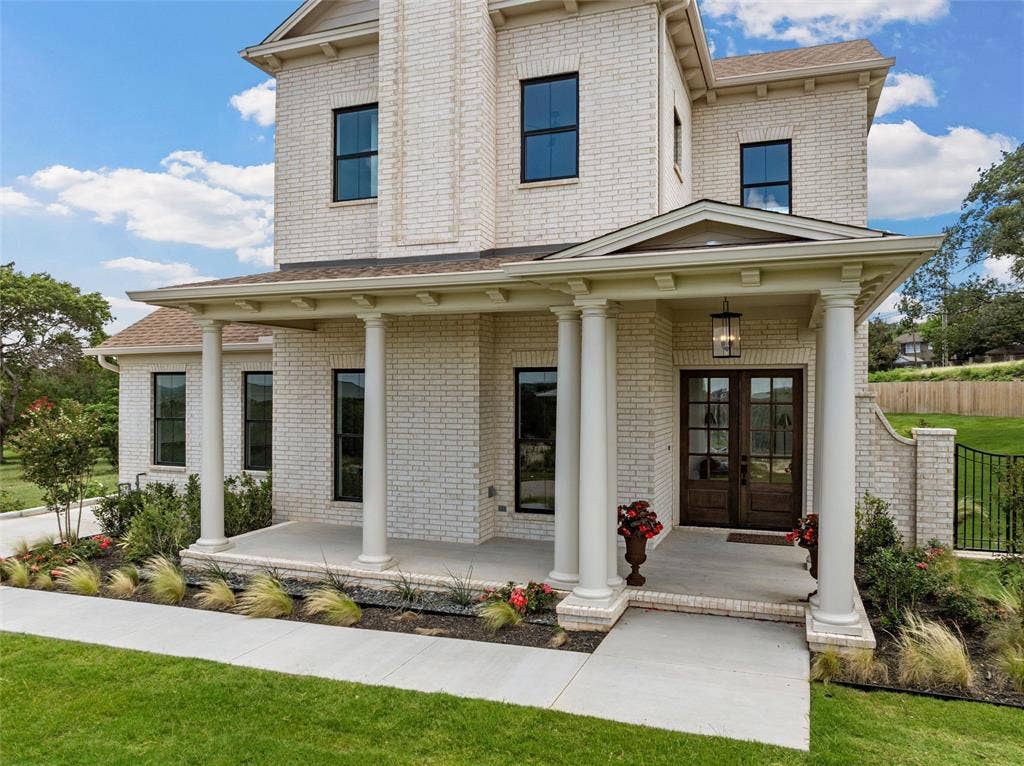 20 N Ritchie Road, Woodway, TX 76712 White brick exterior with black-framed windows, a covered entry porch with columns, dark wood-finish double entry doors, and mature landscaping