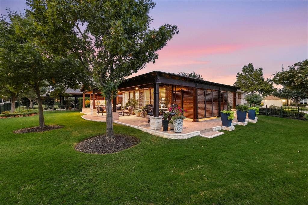 1641 Overwood Drive, Frisco, TX 75036 Expansive lawn space featuring mature trees, a multi-level patio with stone retaining walls, and a covered outdoor living area with wood slat privacy screens