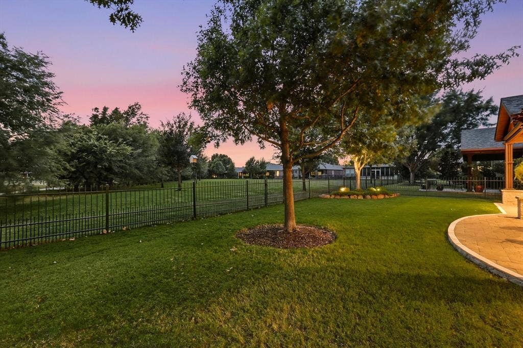 1641 Overwood Drive, Frisco, TX 75036 Expansive lawn with mature trees, a black metal fence, a curved paver patio, and recessed landscape lighting