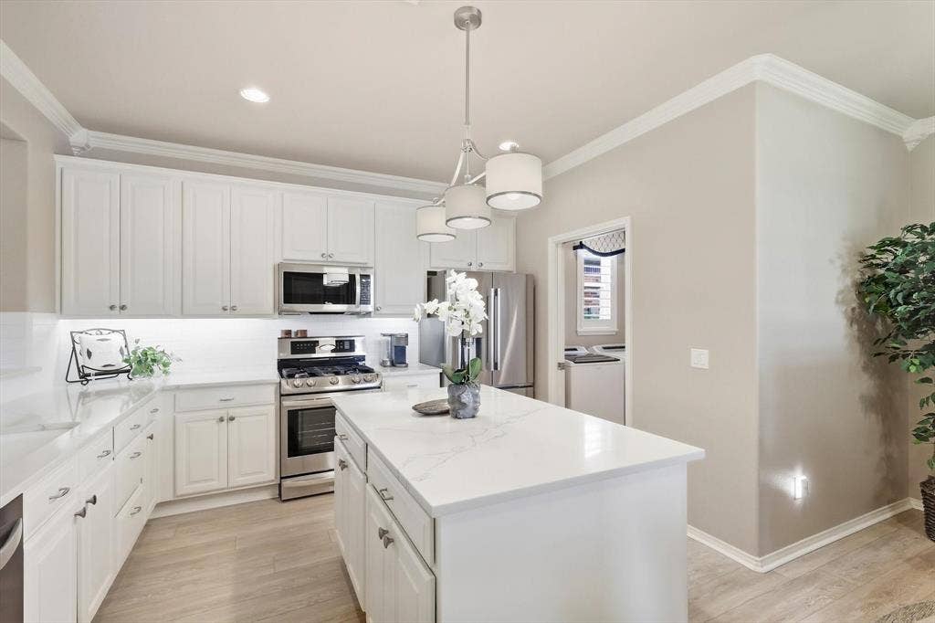 1641 Overwood Drive, Frisco, TX 75036 Kitchen featuring white cabinetry, light-toned countertops, stainless steel appliances, a center island, wood-finish flooring and entry to Utility Room