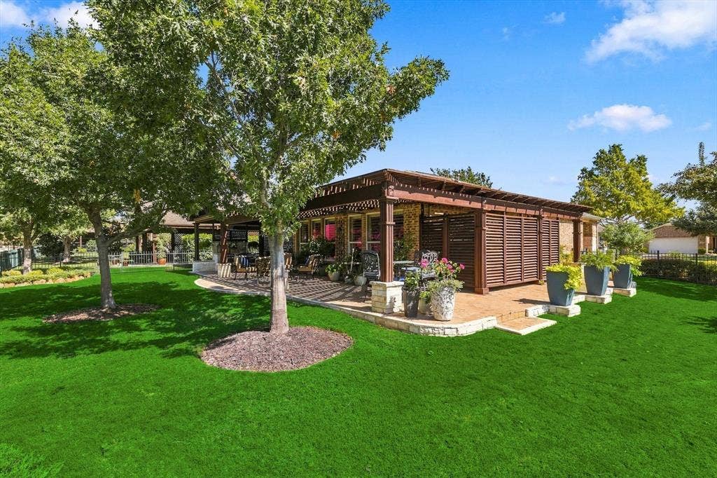 1641 Overwood Drive, Frisco, TX 75036 Green lawn with mature trees, a multi-level stone patio, an extended large wooden pergola, and slatted privacy screening for storage