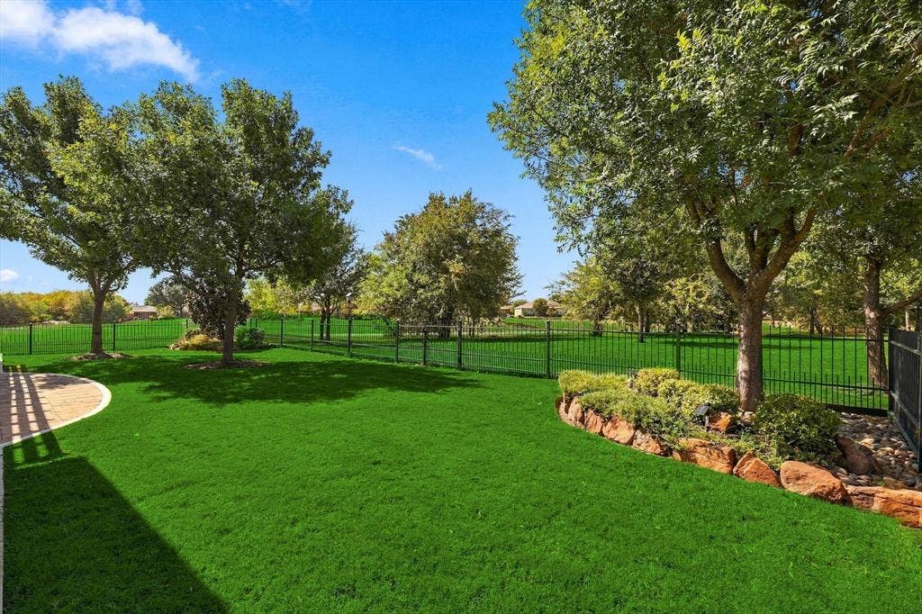 1641 Overwood Drive, Frisco, TX 75036 Green lawn with a view of Greenbelt, a stone-edged garden bed, and a fully fenced back yard with wrought-iron fence
