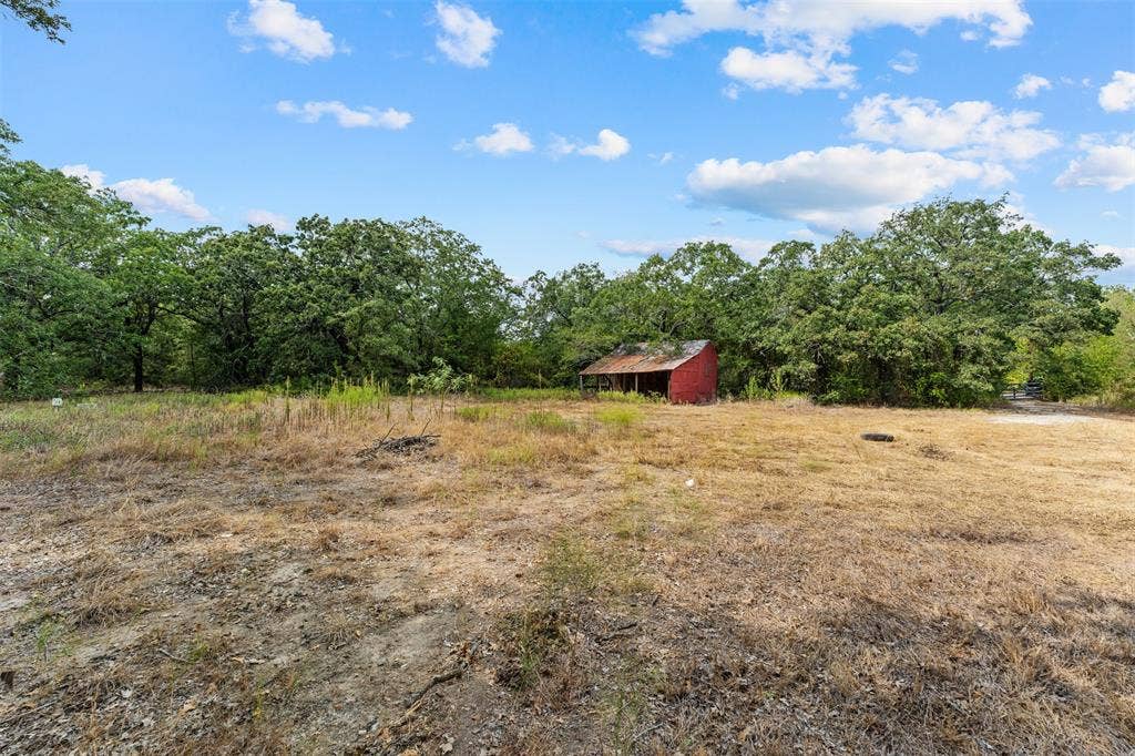 172 M Burton Street, Riesel, TX 76682 Expansive lot featuring mature trees and a rustic red outbuilding