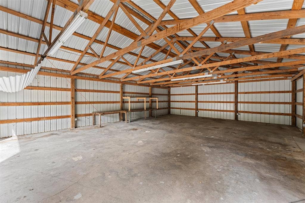 172 M Burton Street, Riesel, TX 76682 Concrete flooring, exposed wood beam ceiling, corrugated metal walls, built-in shelving, and overhead fluorescent lighting