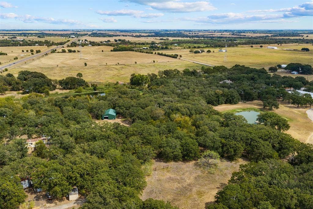 172 M Burton Street, Riesel, TX 76682 Expansive land featuring significant tree coverage, a natural pond, and a green outbuilding