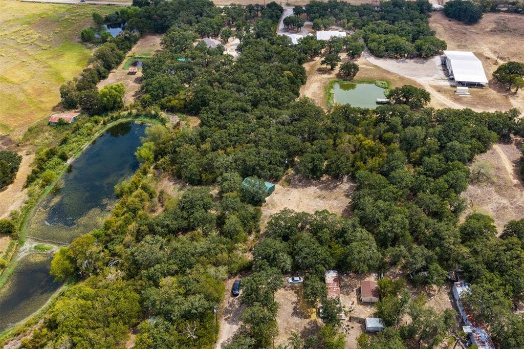 172 M Burton Street, Riesel, TX 76682 Expansive property featuring mature trees, multiple ponds, and a large metal-roofed structure