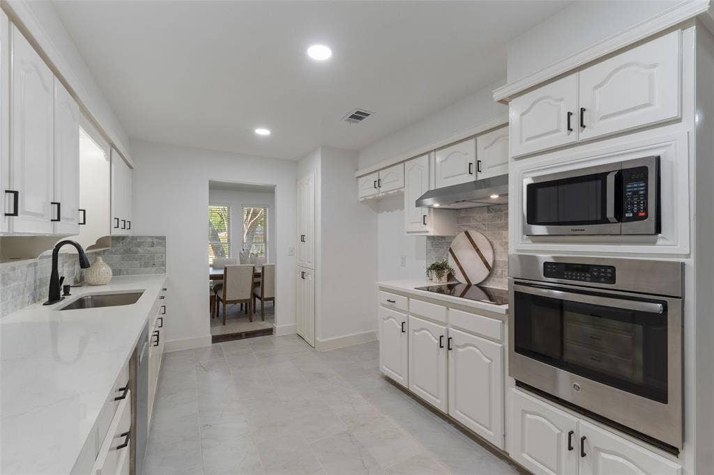 1612 Northcrest Drive, Plano, TX 75075 Kitchen featuring white cabinetry, integrated stainless steel appliances, light-toned countertops, and a tiled backsplash