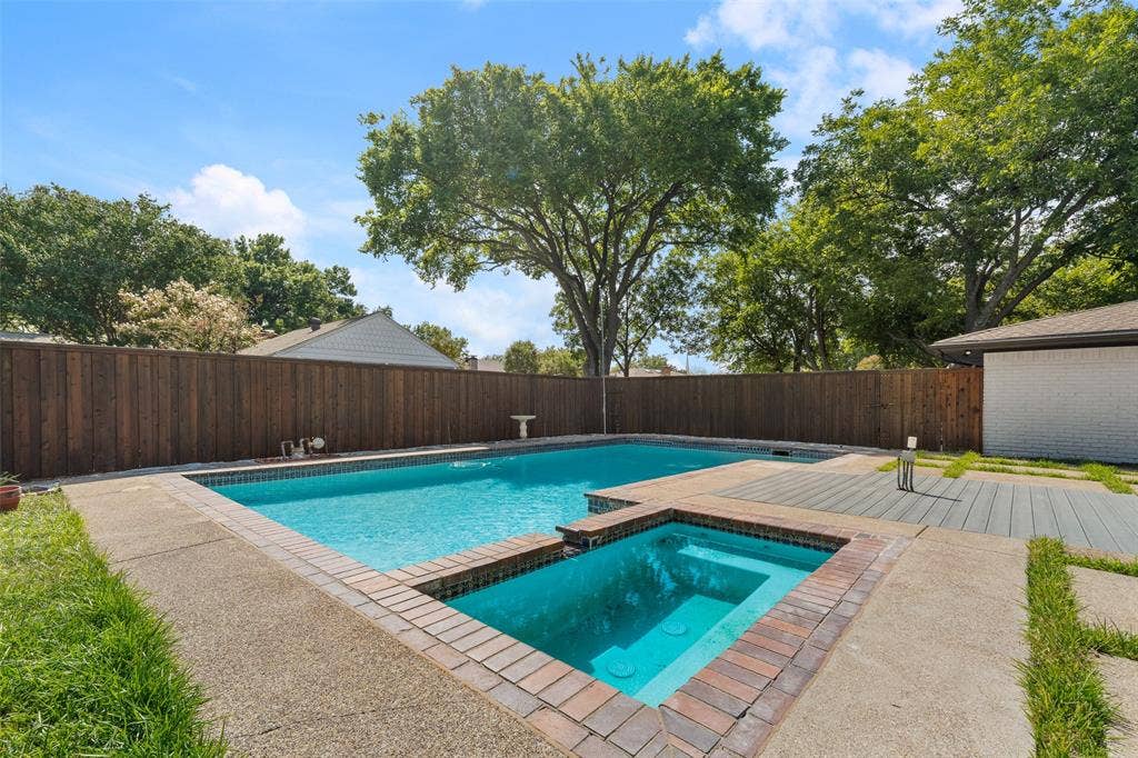 1612 Northcrest Drive, Plano, TX 75075 Swimming pool with an integrated hot tub, surrounded by exposed aggregate concrete decking and brick coping