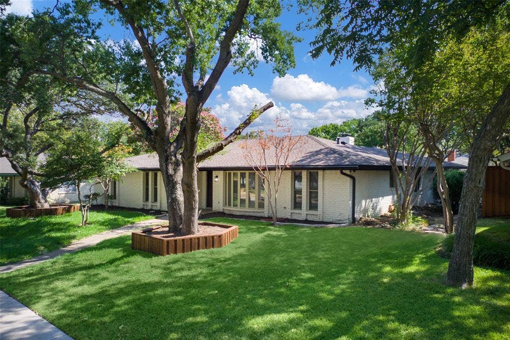 1612 Northcrest Drive, Plano, TX 75075 Exterior featuring a light-colored brick facade, dark-trimmed windows, a dark roof, mature trees, and a concrete pathway