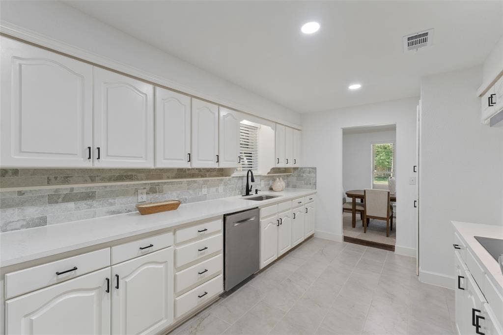 1612 Northcrest Drive, Plano, TX 75075 White cabinetry with black hardware, light-toned countertops, a light-toned tile backsplash, and stainless steel appliances
