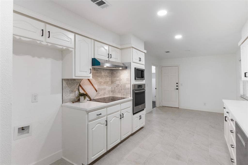 1612 Northcrest Drive, Plano, TX 75075 White cabinetry with black hardware, stainless steel built-in oven and microwave, stone-finish backsplash, recessed lighting, and large format tile flooring